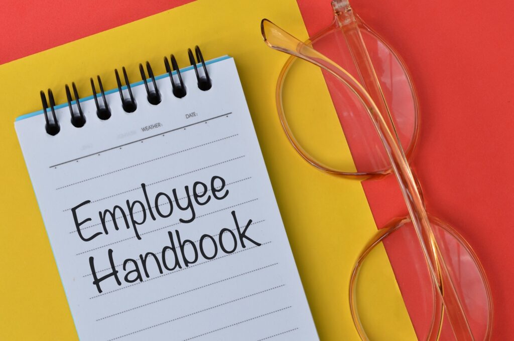 Top view of eyeglasses and notebook written with text EMPLOYEE HANDBOOK